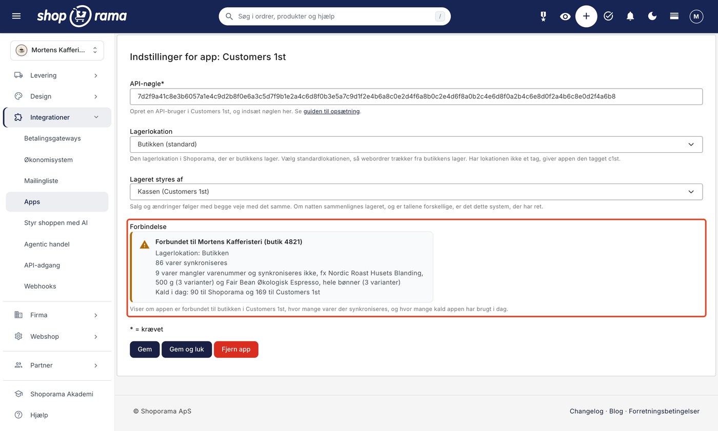 Indstillinger for app: Customers 1st med statusboksen Forbindelse markeret. Boksen har et gult advarselsikon og overskriften Forbundet til Mortens Kafferisteri (butik 4821), og under den linjerne Lagerlokation: Butikken, 86 varer synkroniseres, 9 varer mangler varenummer og synkroniseres ikke, fx Nordic Roast Husets Blanding, 500 g (3 varianter) og Fair Bean Økologisk Espresso, hele bønner (3 varianter), og Kald i dag: 90 til Shoporama og 169 til Customers 1st.